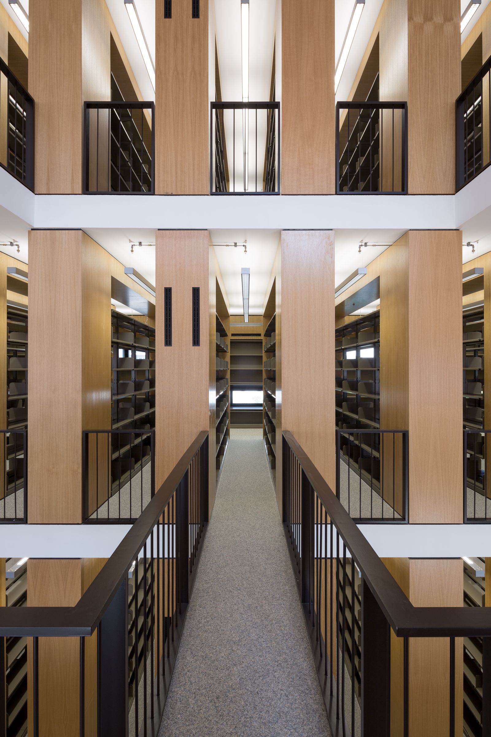 Blick über eine Brücke auf mehrere Galerieebenen einer Bibliothek mit Holzregalen