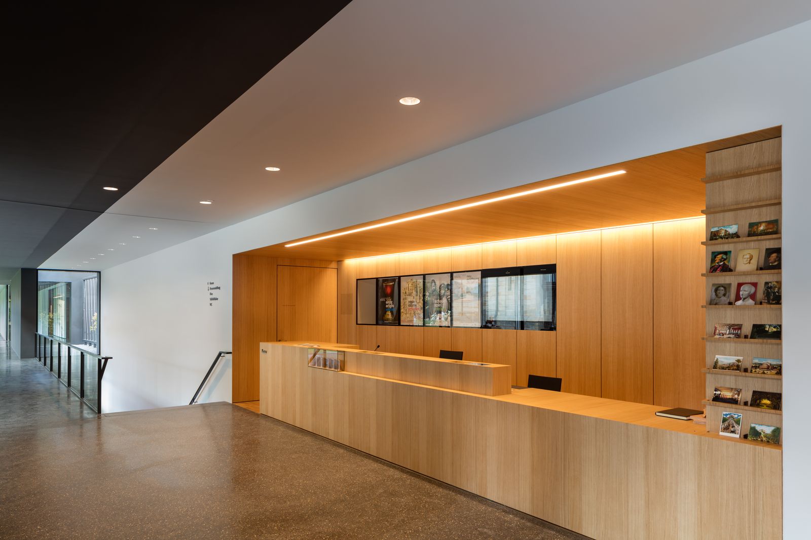 Empfangstresen und Wandverkleidung aus hellem Holz mit Regalen im Museumsfoyer