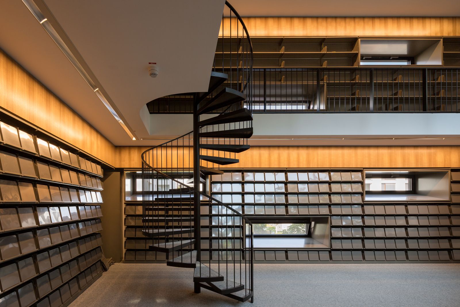 Raumhohe Regalwand aus Holz mit schwarzer Wendeltreppe zur Galerie