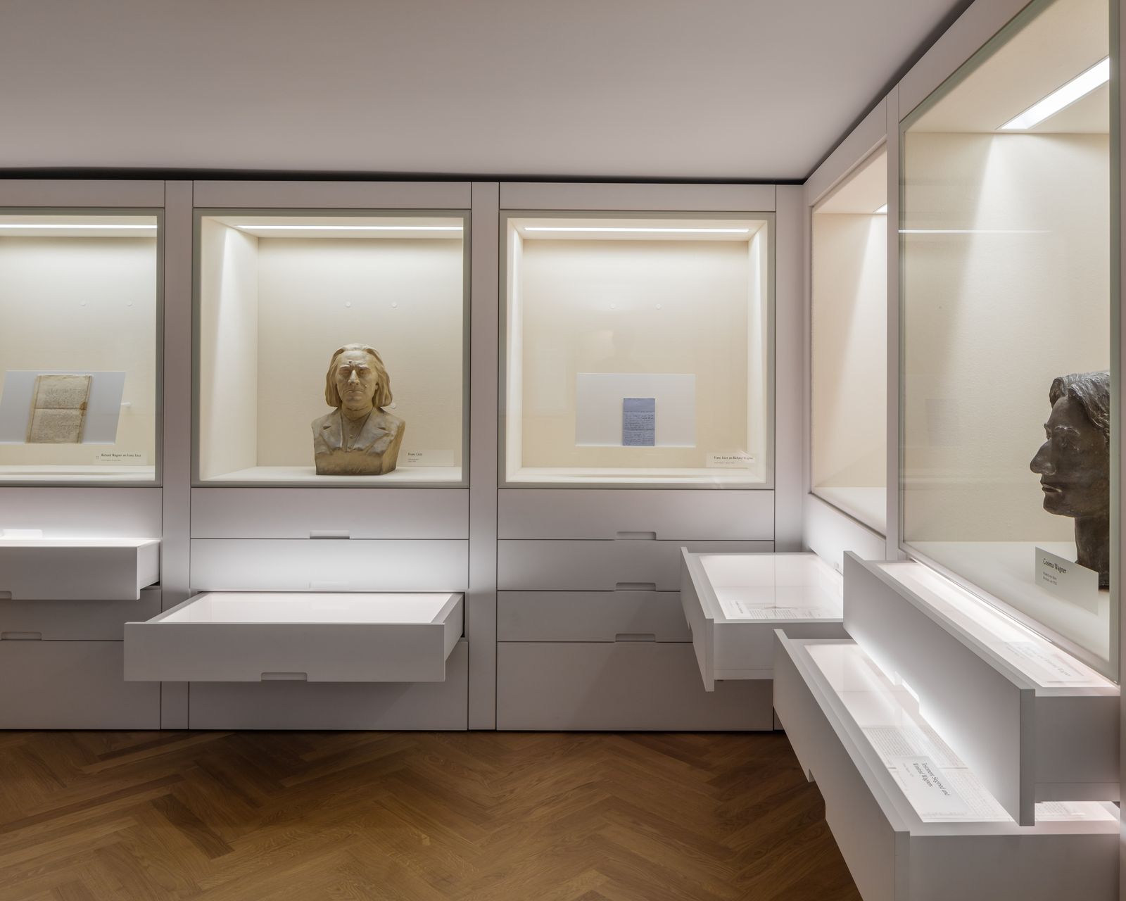 Beleuchtete Wandvitrinen mit Büsten und Exponaten auf weißen Ausstellungsmöbeln
