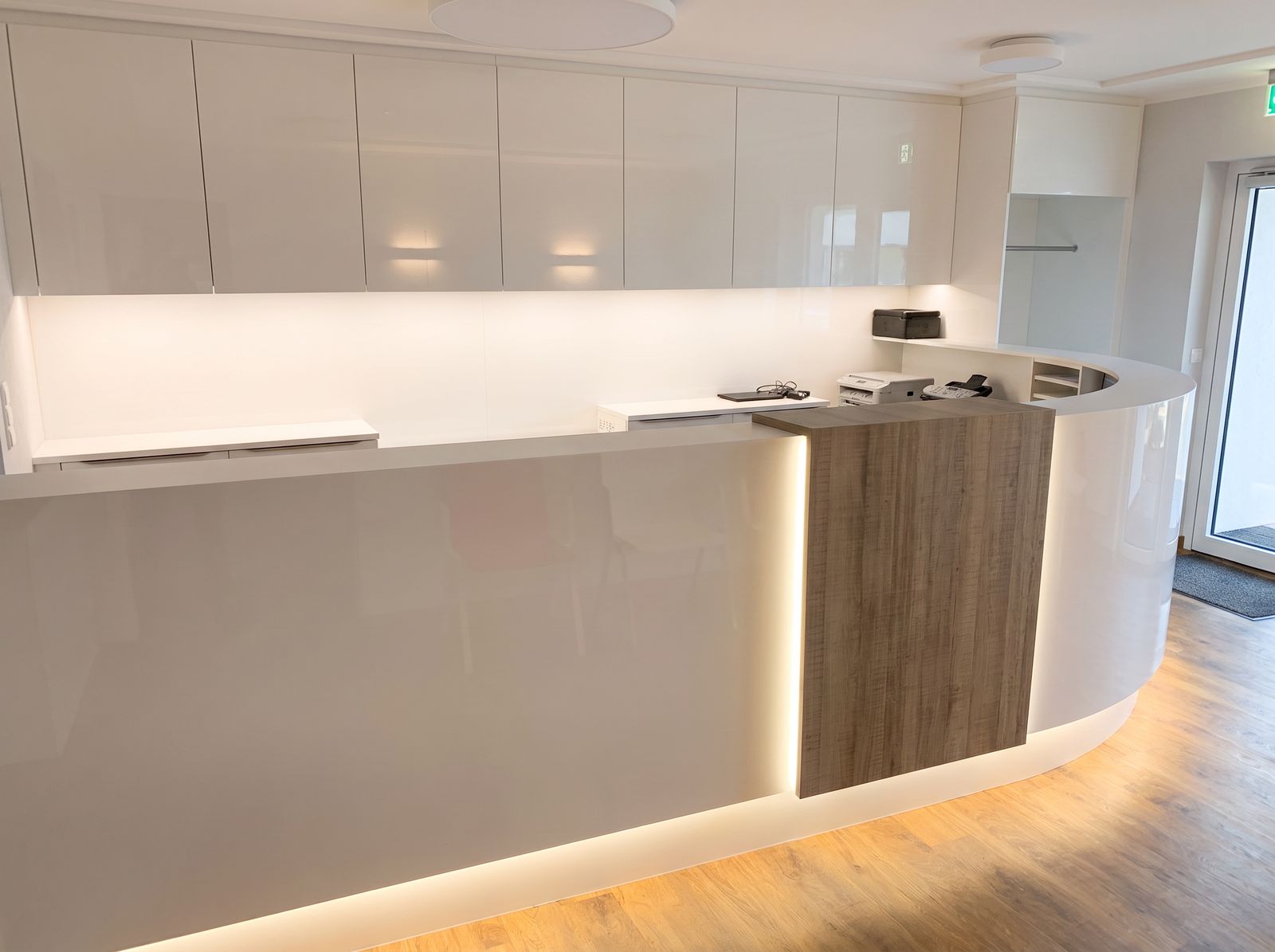 Geschwungene Empfangstheke in Beige-Hochglanz mit Holzblende und indirekter LED-Beleuchtung