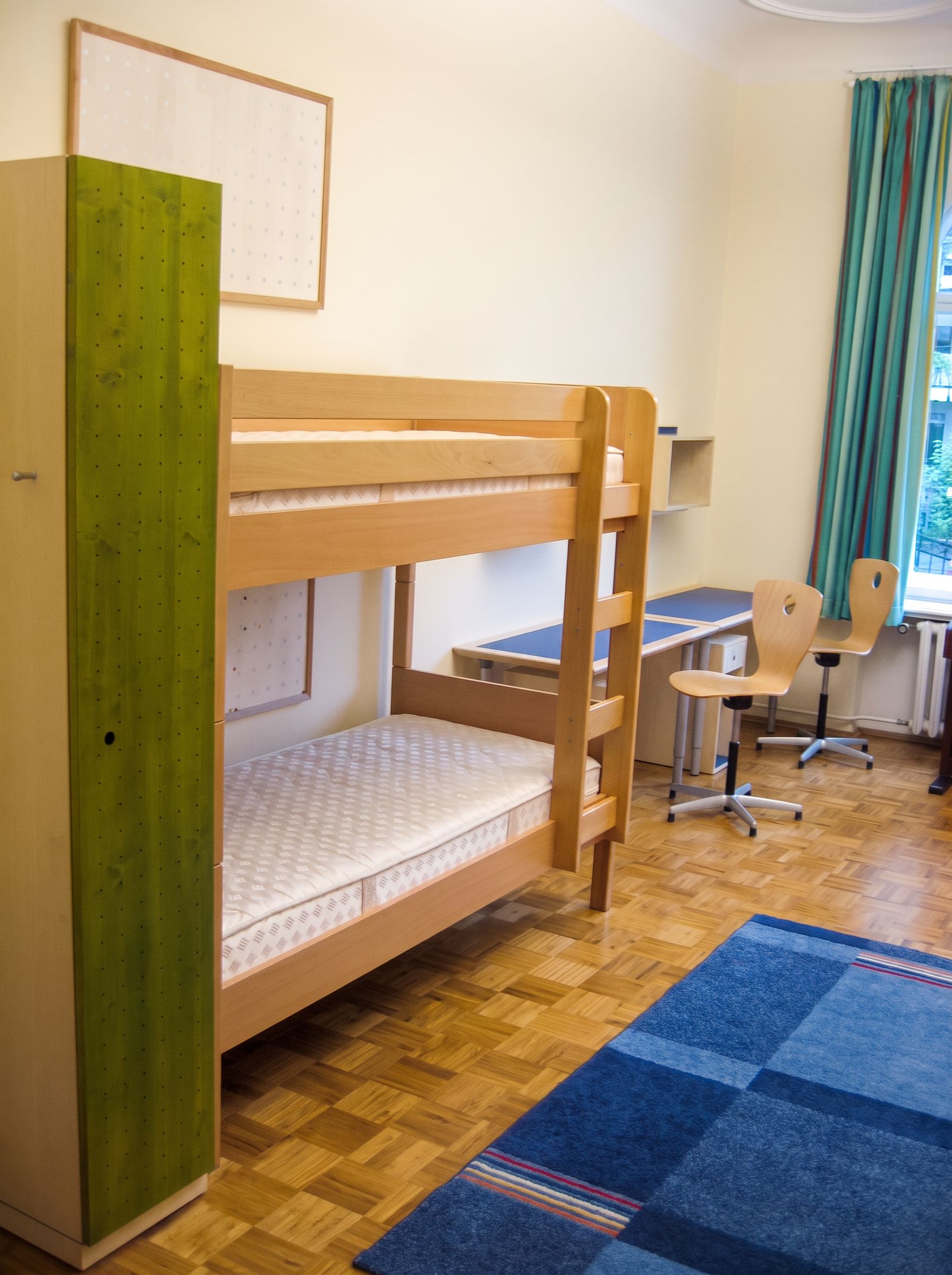 Etagenbett aus Massivholz Buche mit grünem Kleiderschrank, Schreibtisch und blauem Teppich im Kinderzimmer