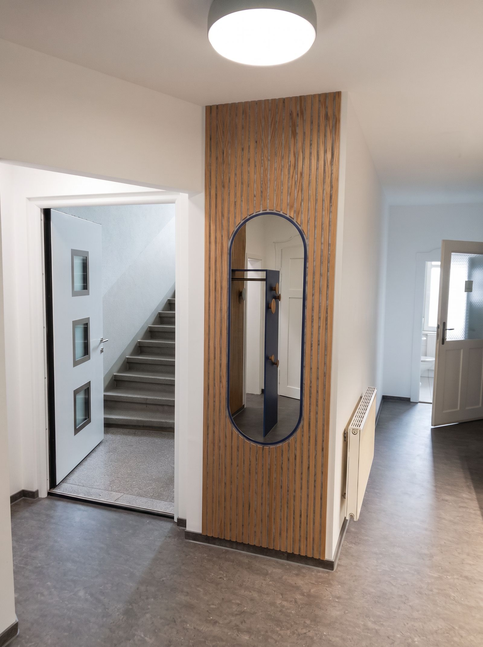 Flur mit Eichen-Lamellenwand und eingelassenem ovalem Spiegel, Blick zum Treppenhaus