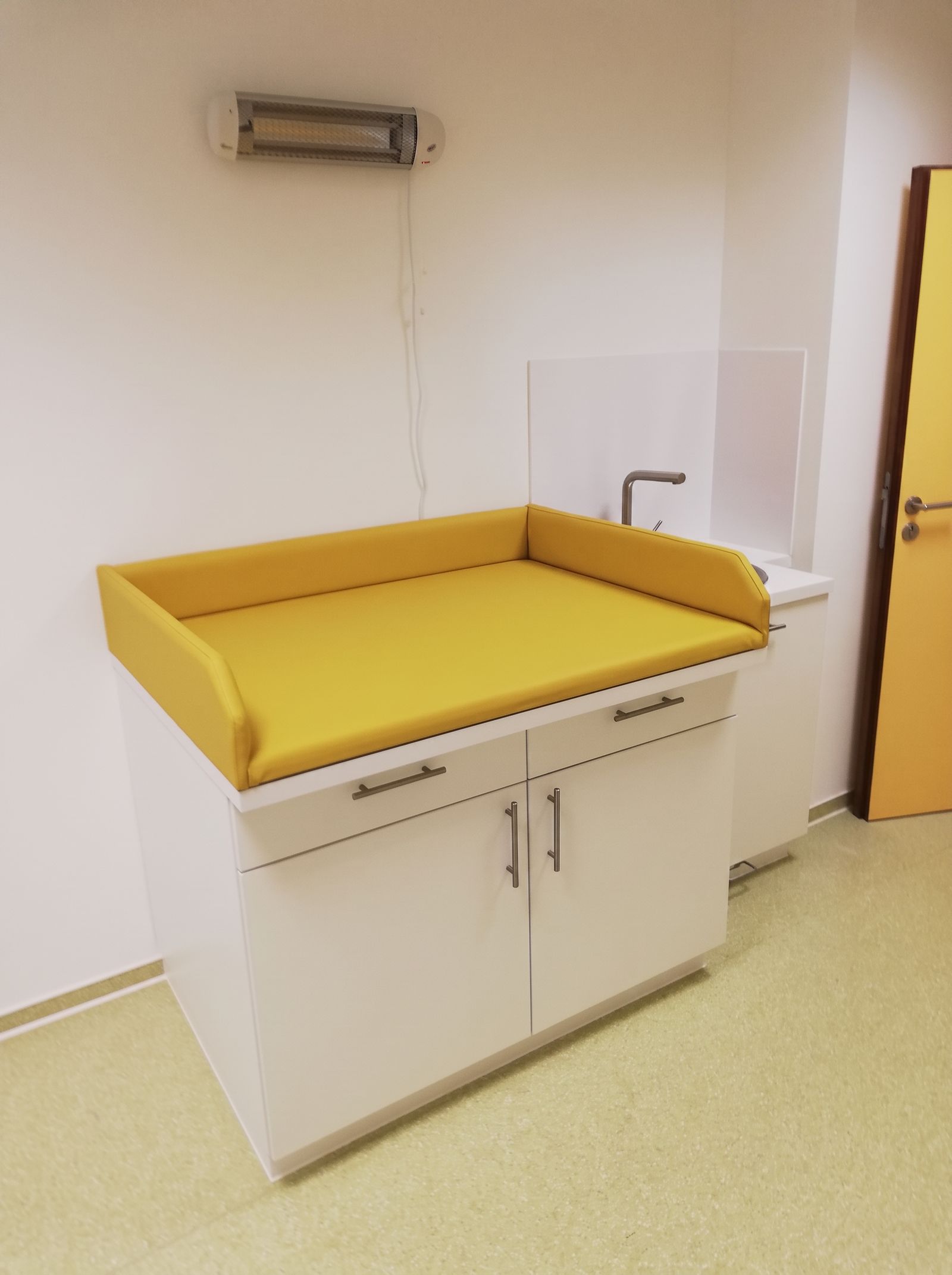 Weißer Wickeltisch mit gelber Wickelauflage, Schubladen und integriertem Waschbecken in einer Kita