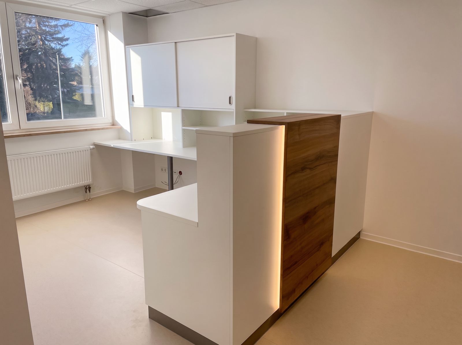 Weiße Theke mit Nussbaum-Paneel und LED-Licht, dahinter Arbeitsplatz mit Schiebetürenschrank