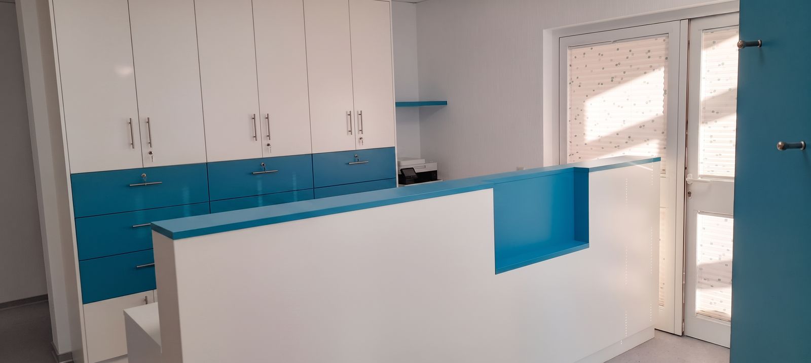 Einbauküche in Weiß mit blauen Hochglanzfronten, Edelstahlgriffen und Thekenblock
