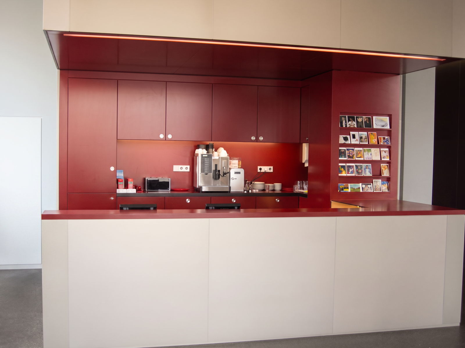 Teeküche in Dunkelrot mit Oberschränken, Kaffeemaschine, LED-Lichtband und heller Thekenfront
