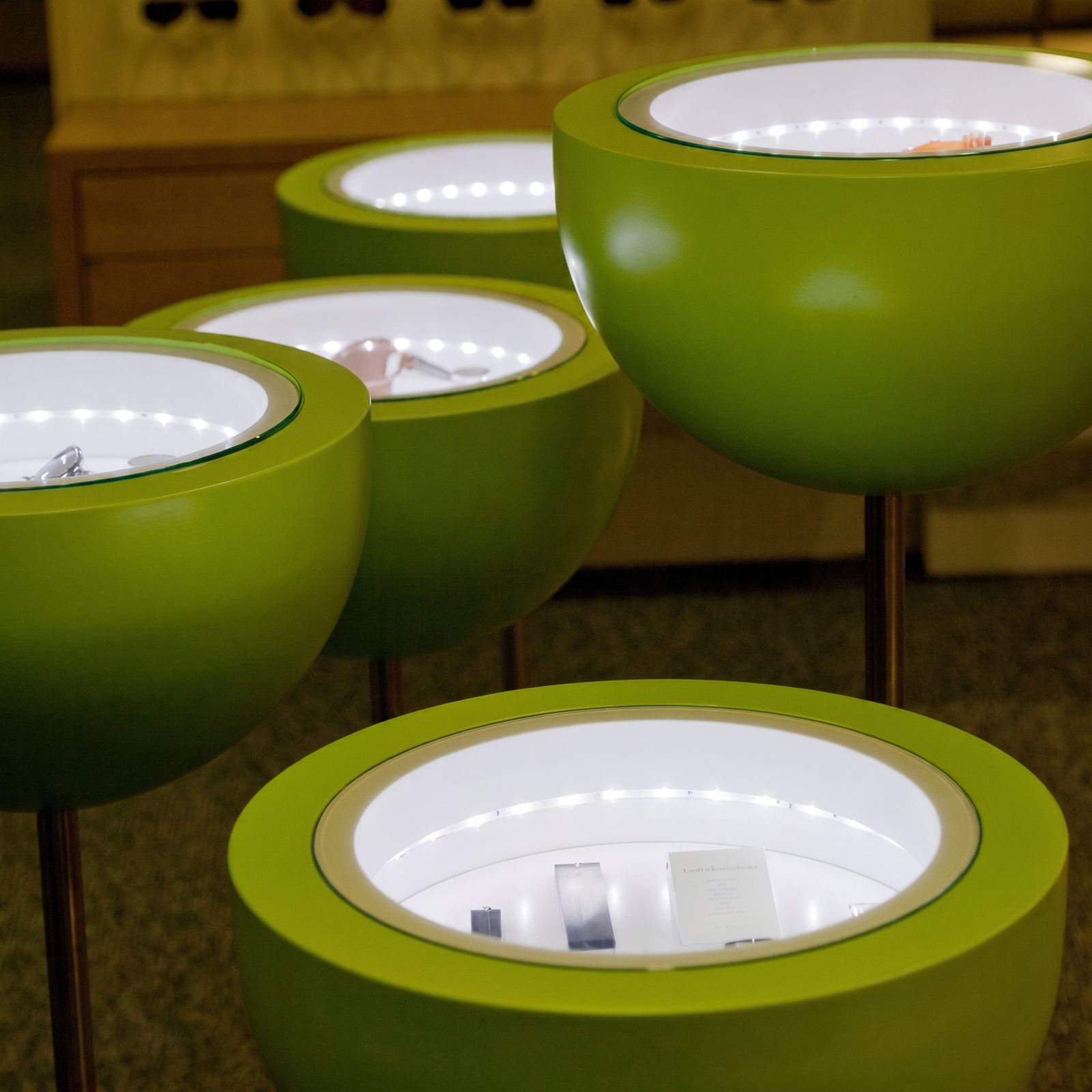 Runde grüne Präsentationsvitrinen auf Stelen mit LED-Beleuchtung und Glasabdeckung im Optikergeschäft