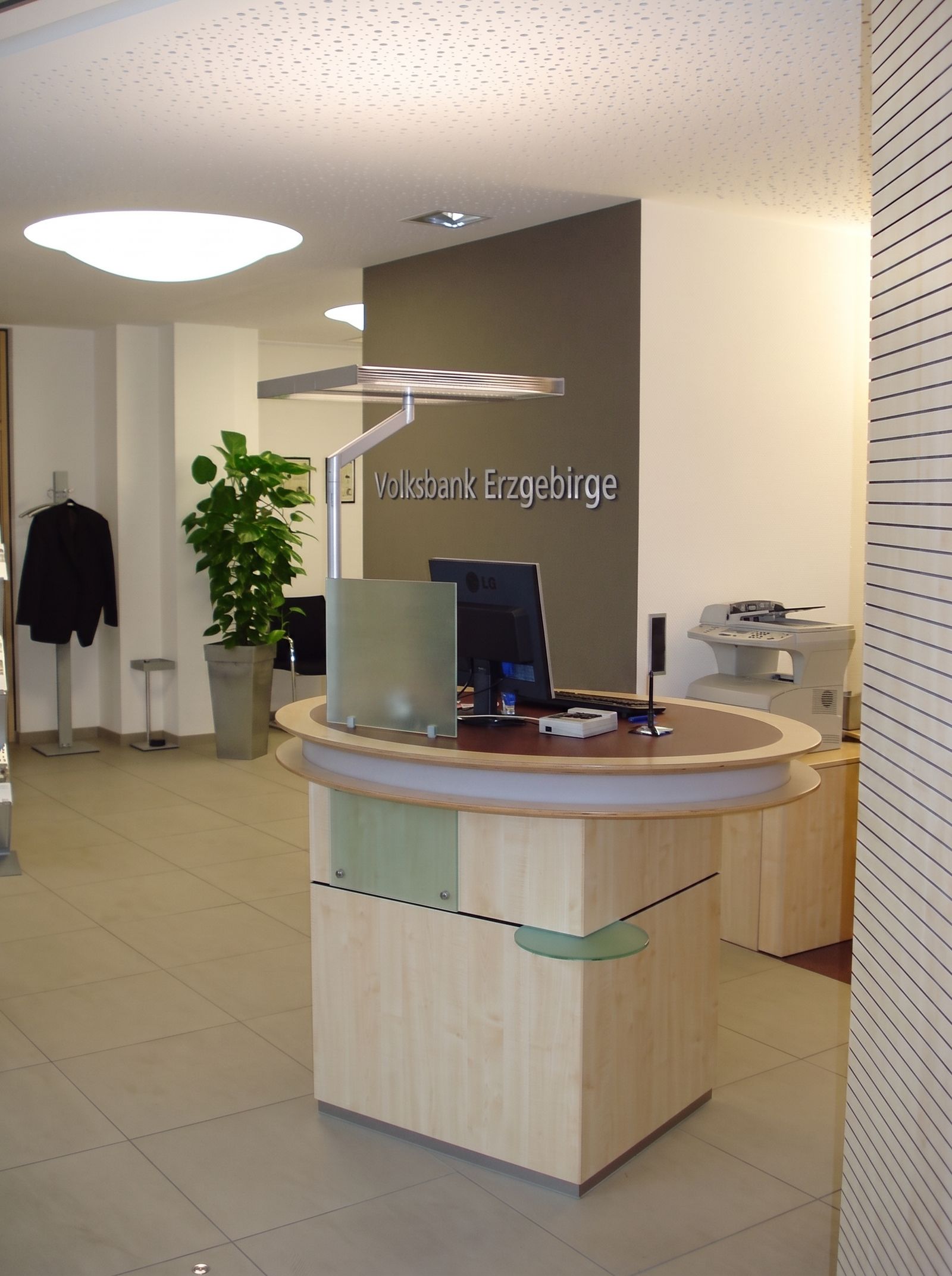 Runde Empfangstheke aus Ahorn mit Glaselement in einer Volksbank-Filiale, Schriftzug an der Wand