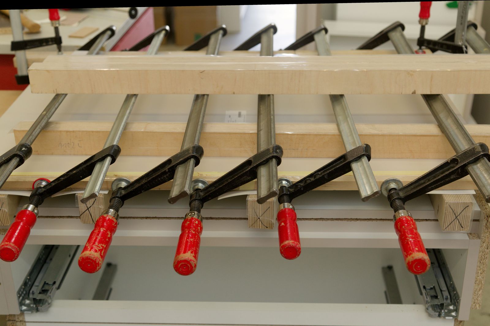 Mehrere Schraubzwingen pressen ein verleimtes Werkstück aus Holzplatten