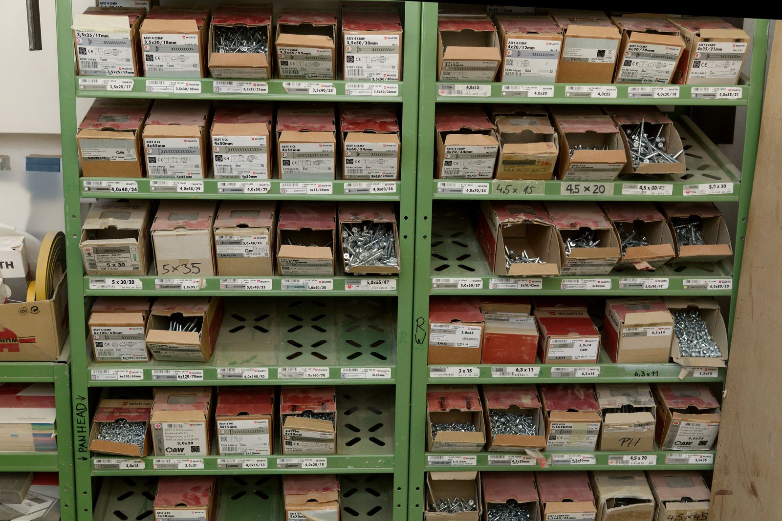 Grünes Lagerregal mit beschrifteten Kartons voller Schrauben